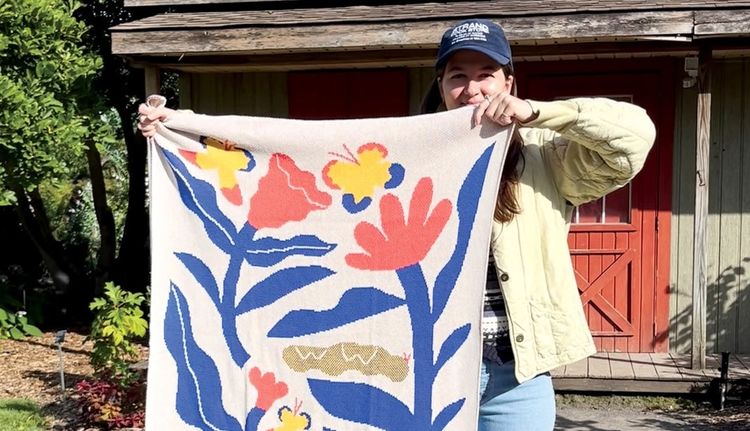 Artist Amelie Lehoux holding up her mini kids knit blanket for babies and nursery with an abstract design of butterflies and flowers