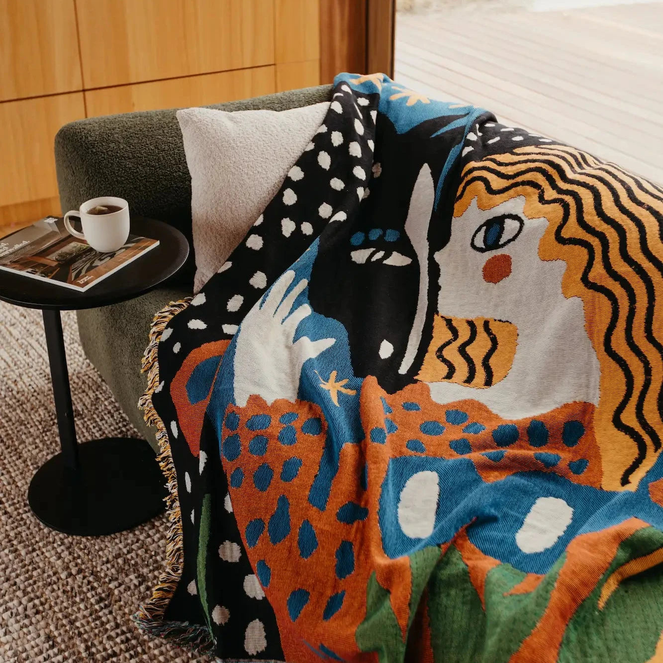 Colorful abstract-patterned blanket draped over a chair with a side table in the background.