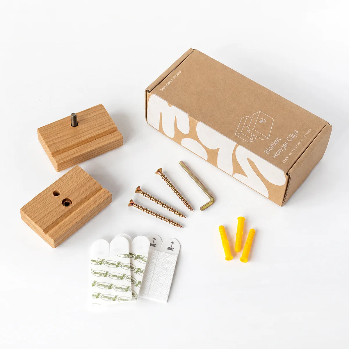 A blanket hanger set of 3 clips in oak with a kit laid out on a white background, including 3 screws, 3 wall anchors, 3 white adhesive hooks, an Allen key and a brown packaging box.