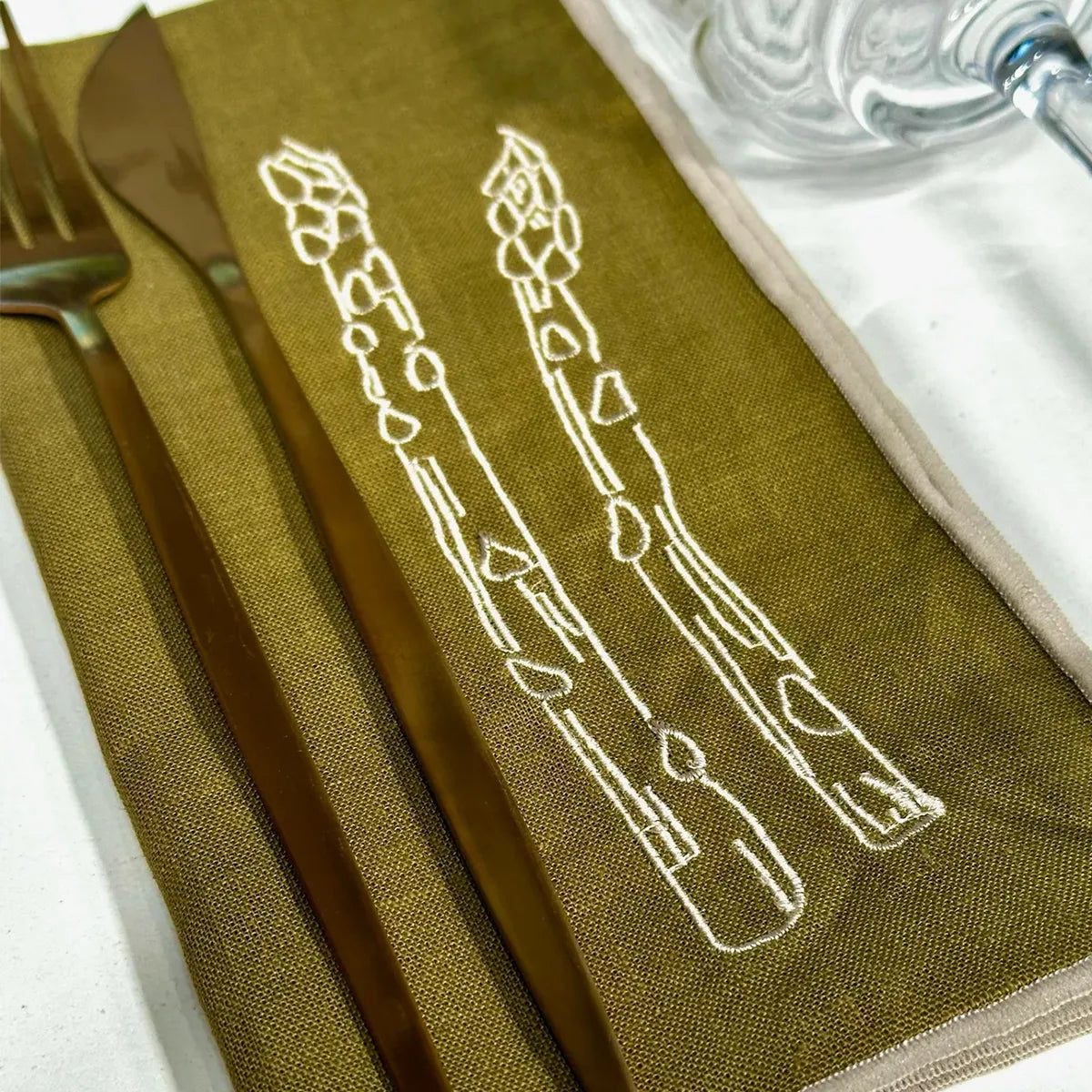 Green napkin with white asparagus design and silverware on a white surface