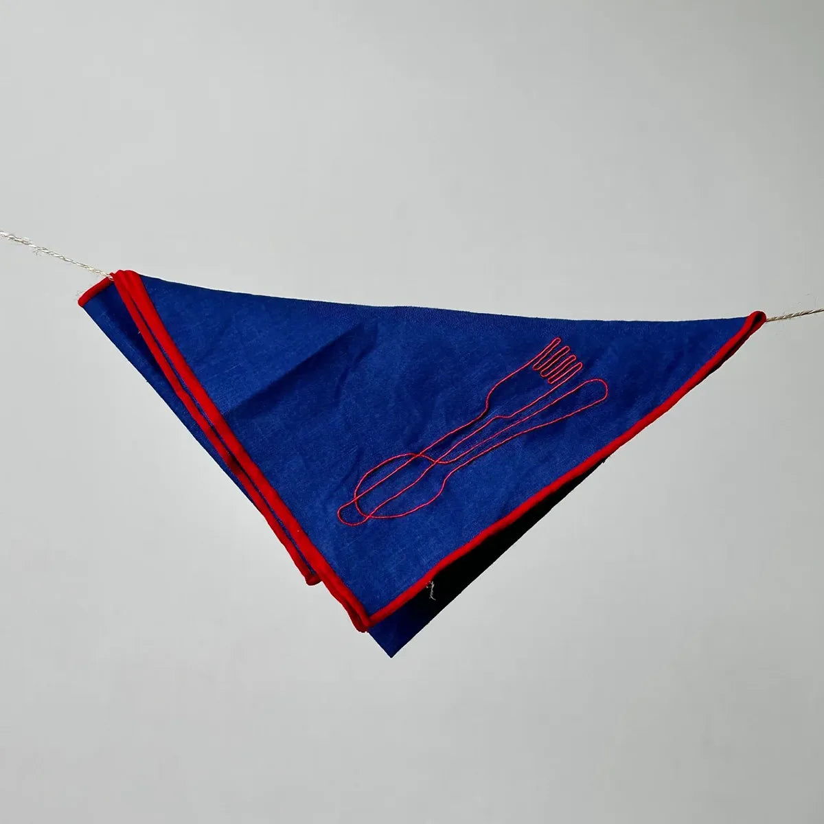 Blue napkin with red trim and embroidered design on a gray background