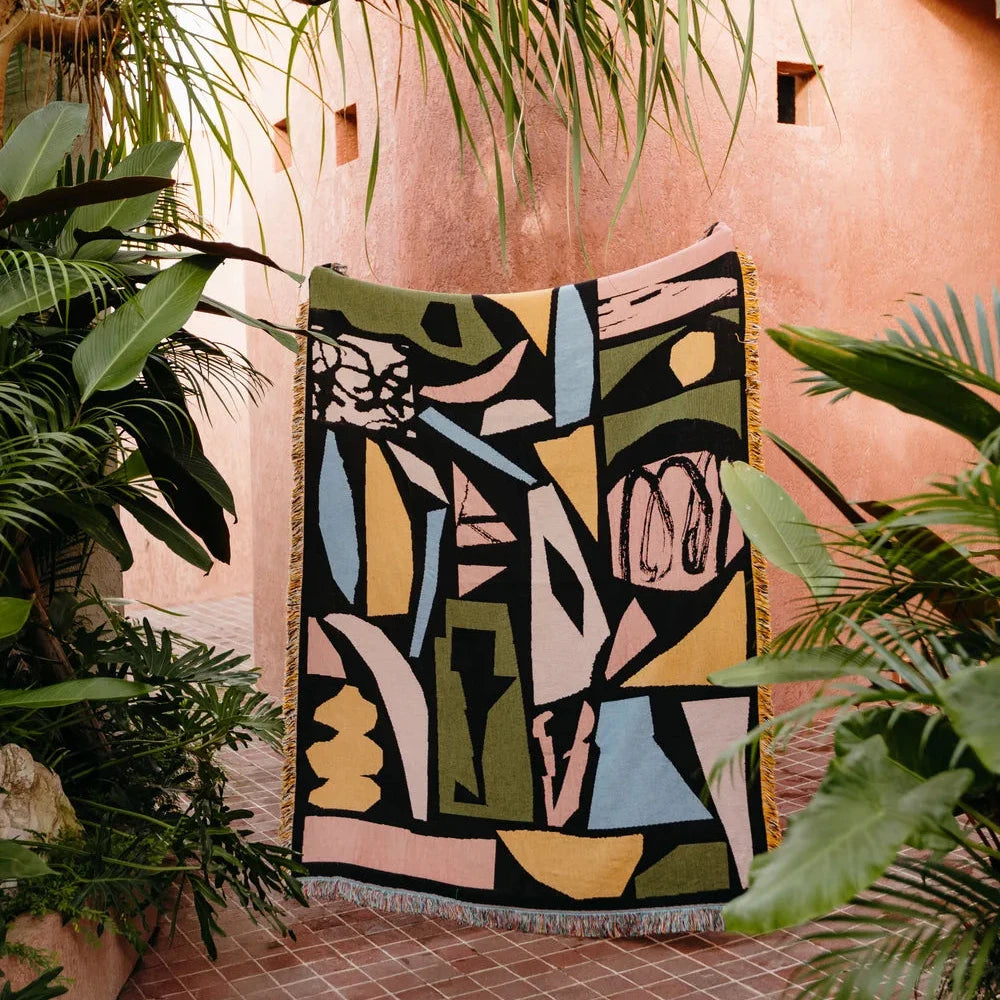 Abstract patterned throw on a pink wall with plants around
