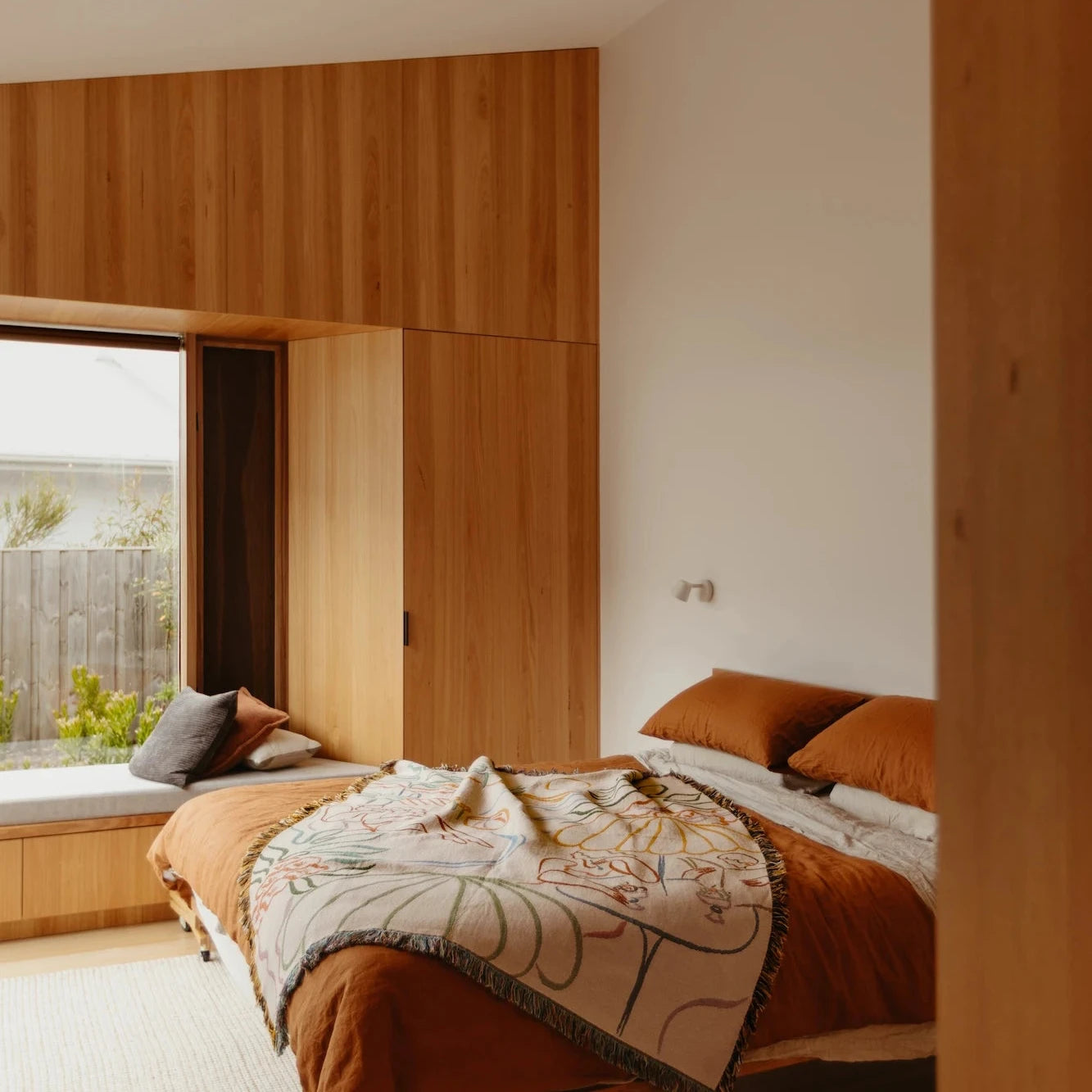 Modern bedroom with wooden walls and a bed with patterned blanket.