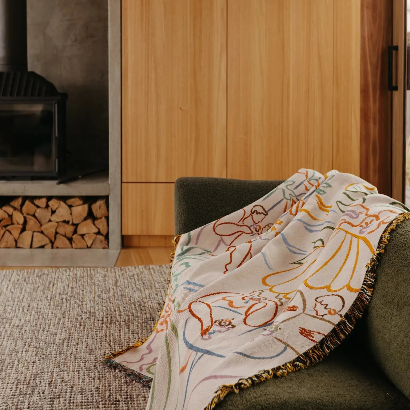 Decorative blanket with patterns draped over a green armchair in a room with wooden walls and a fireplace.