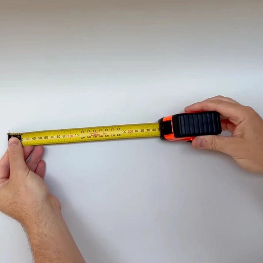 Person using a tape measure on a white surface to hang a tapestry on wall. Measuring wall hanging
