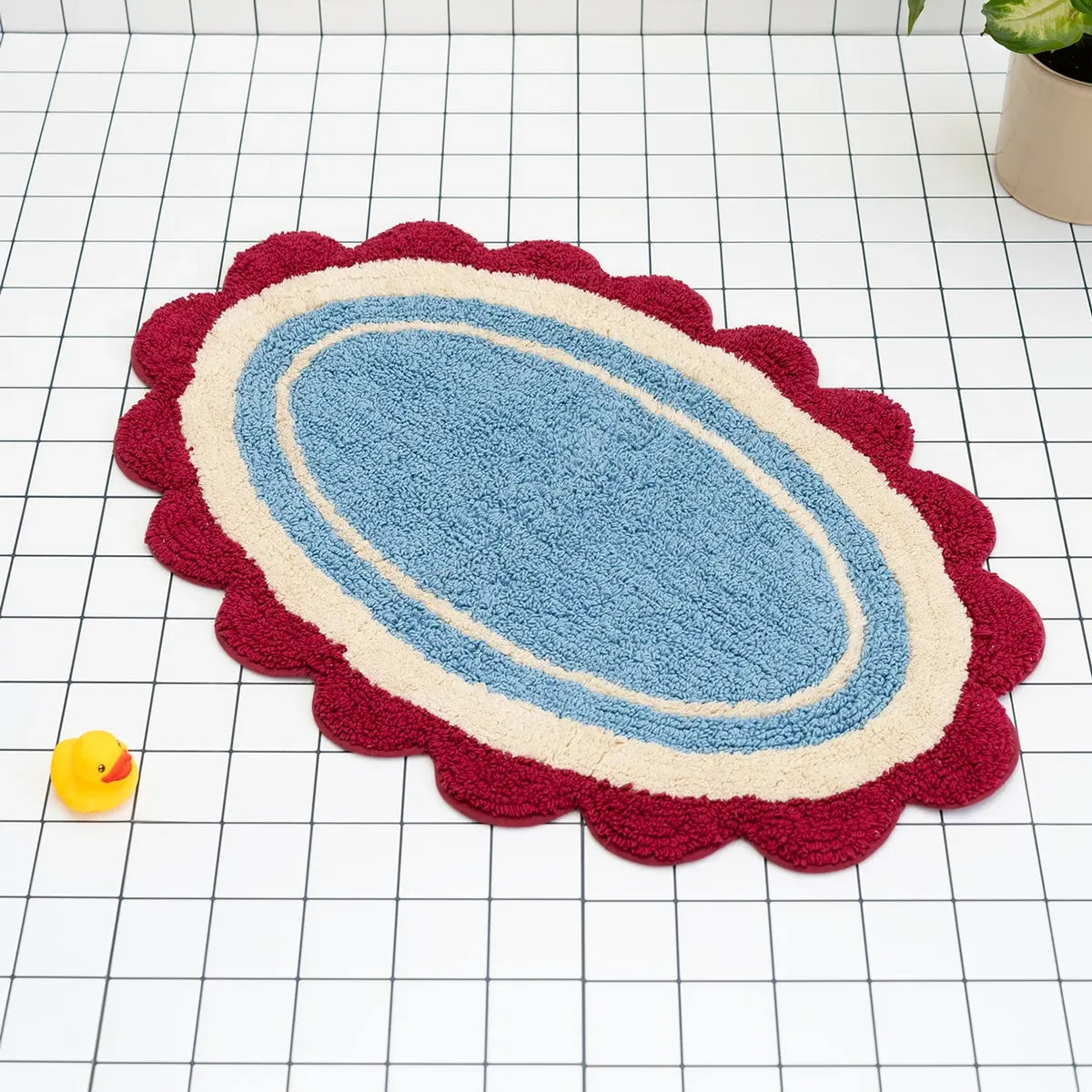 Blue bath mat with red and beige scalloped edge on a grid background