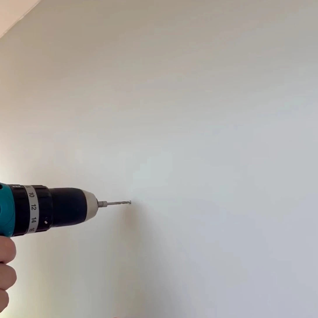Hand holding a drill with a screw bit into the wall for tapestry wall hanging