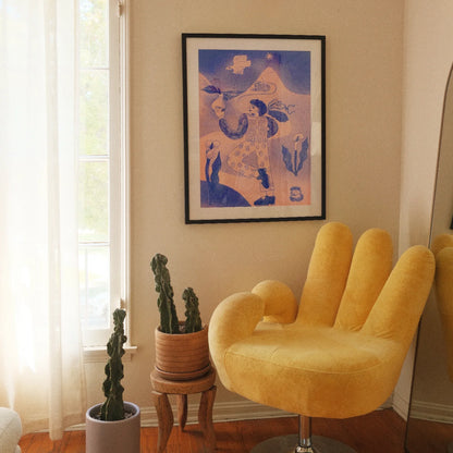 A framed art print featuring a stylized figure in blue and cream tones, displayed on a beige wall in a room with a yellow hand-shaped chair, potted cacti, and a window.
