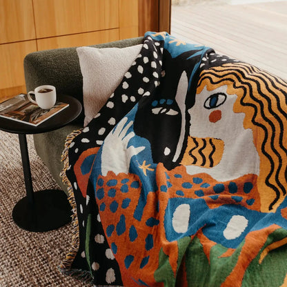Colorful abstract-patterned blanket draped over a chair with a side table in the background.