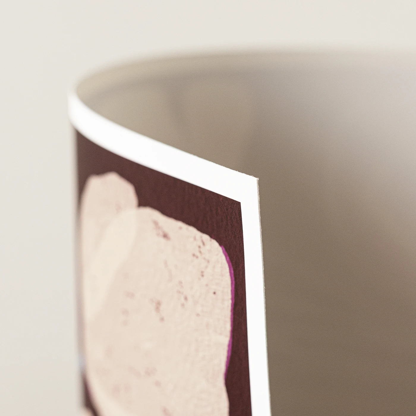 A close-up of an art print, showing a dark burgundy background with a large pale pink abstract shape and a white border, photographed against a soft light gray background.