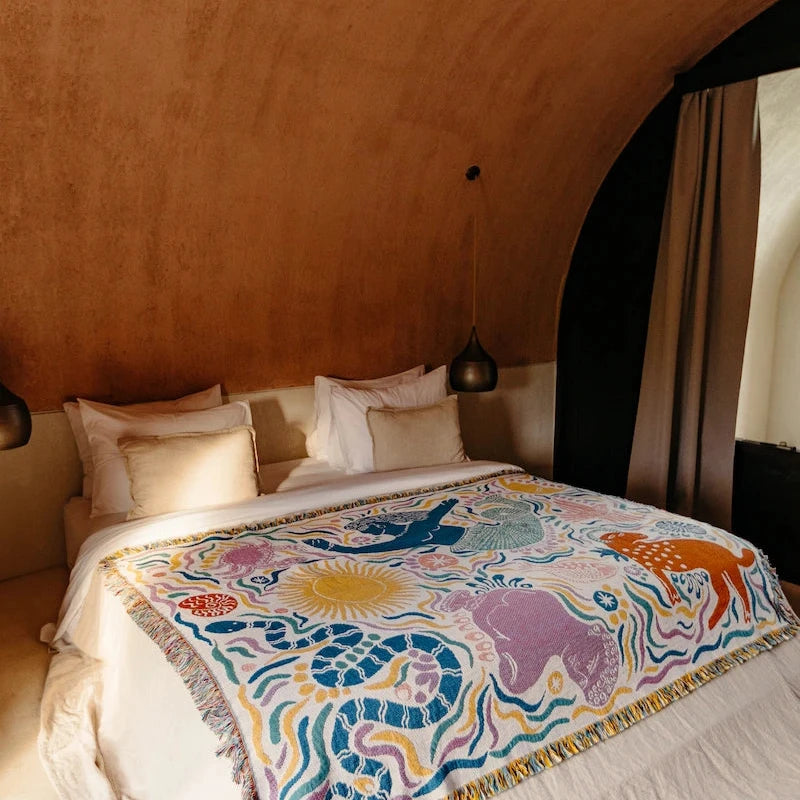 Bed with a colorful blanket featuring mythical greek animals in a bedroom setting.