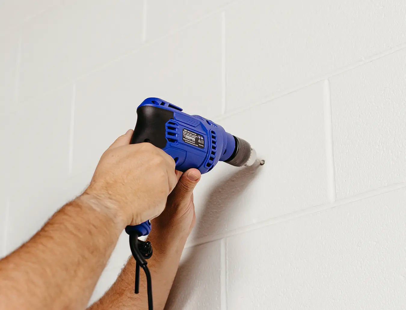 Person drilling a hole in a masonry wall. 