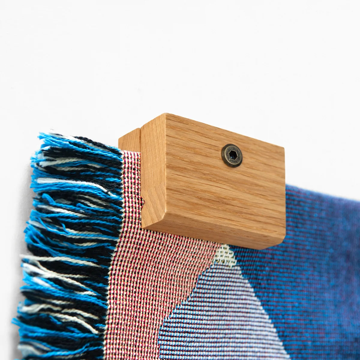 Close up image of a corner of a Slowdown woven blanket being held up on a wall with an Oak blanket hanger clip.