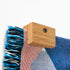 Close up image of a corner of a Slowdown woven blanket being held up on a wall with an Oak blanket hanger clip.