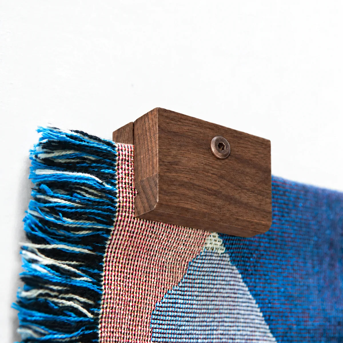 Close up image of a corner of a Slowdown woven blanket being held up on a wall with an walnut blanket hanger clip.
