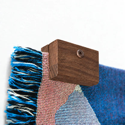 Close up image of a corner of a Slowdown woven blanket being held up on a wall with an walnut blanket hanger clip.