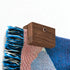 Close up image of a corner of a Slowdown woven blanket being held up on a wall with an walnut blanket hanger clip.