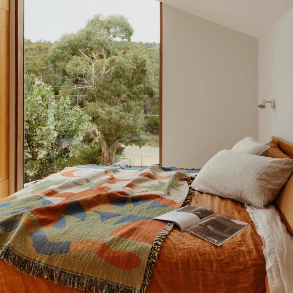 Bedroom with a large window view of trees and orange and green throw blanket with desert design