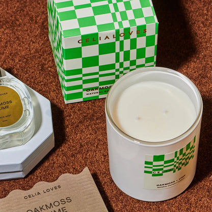 Candle with green and white checkered design, next to a green and white box on a brown surface.