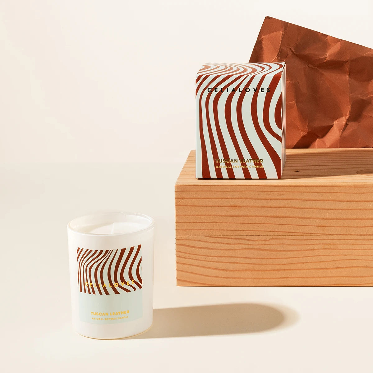 Candle with wavy stripes and matching packaging on a wooden plinth on a light background