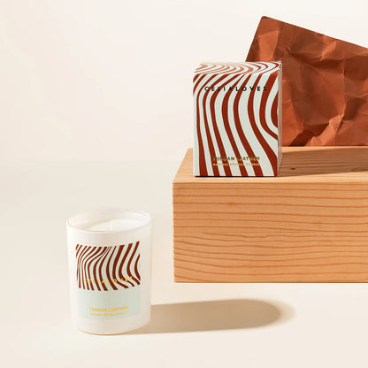 Candle with wavy stripes and matching packaging on a wooden plinth on a light background