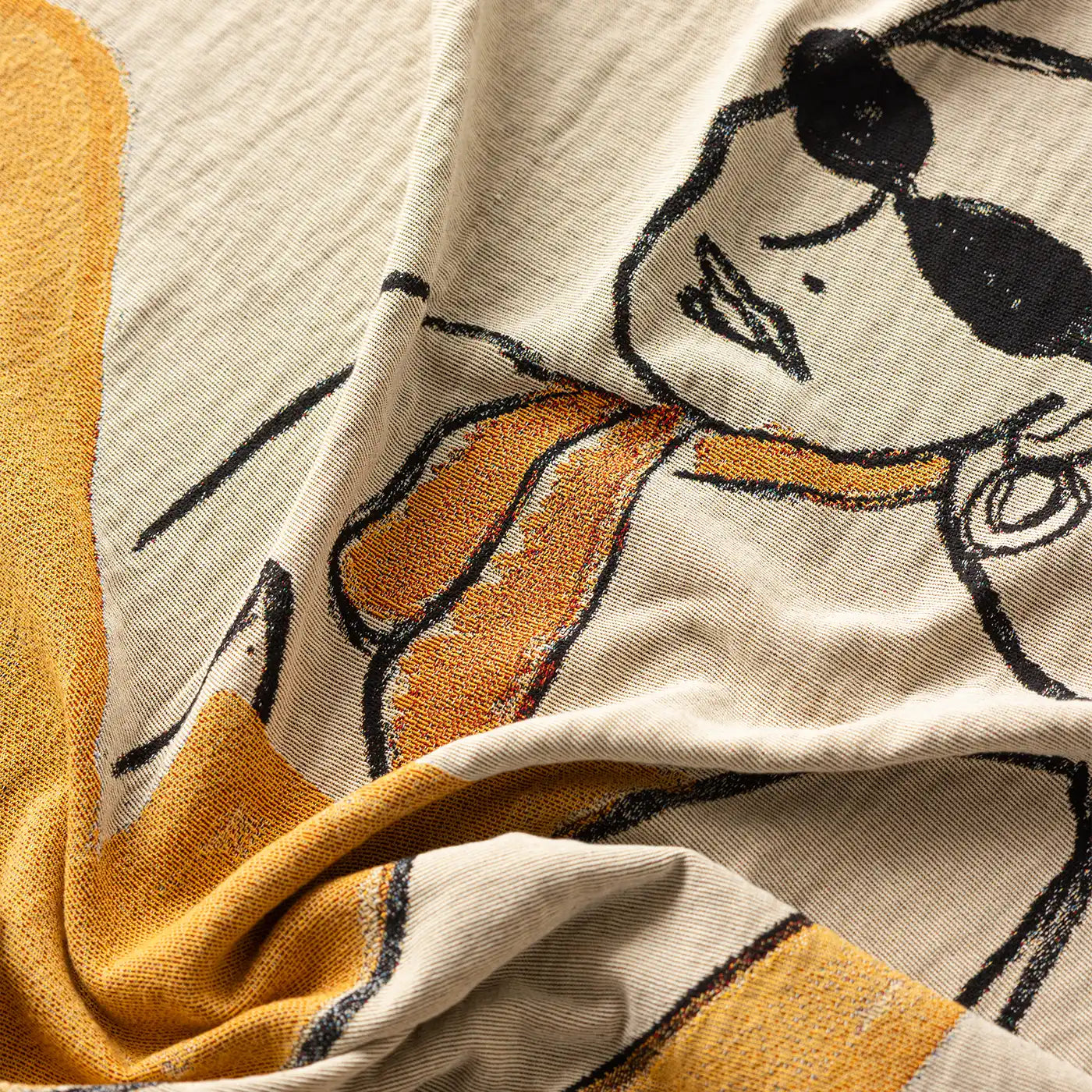 A close-up of a textured cream-colored fabric with a stylized graphic print of a woman wearing black sunglasses and a mustard yellow scarf, accented with a wide mustard yellow border.