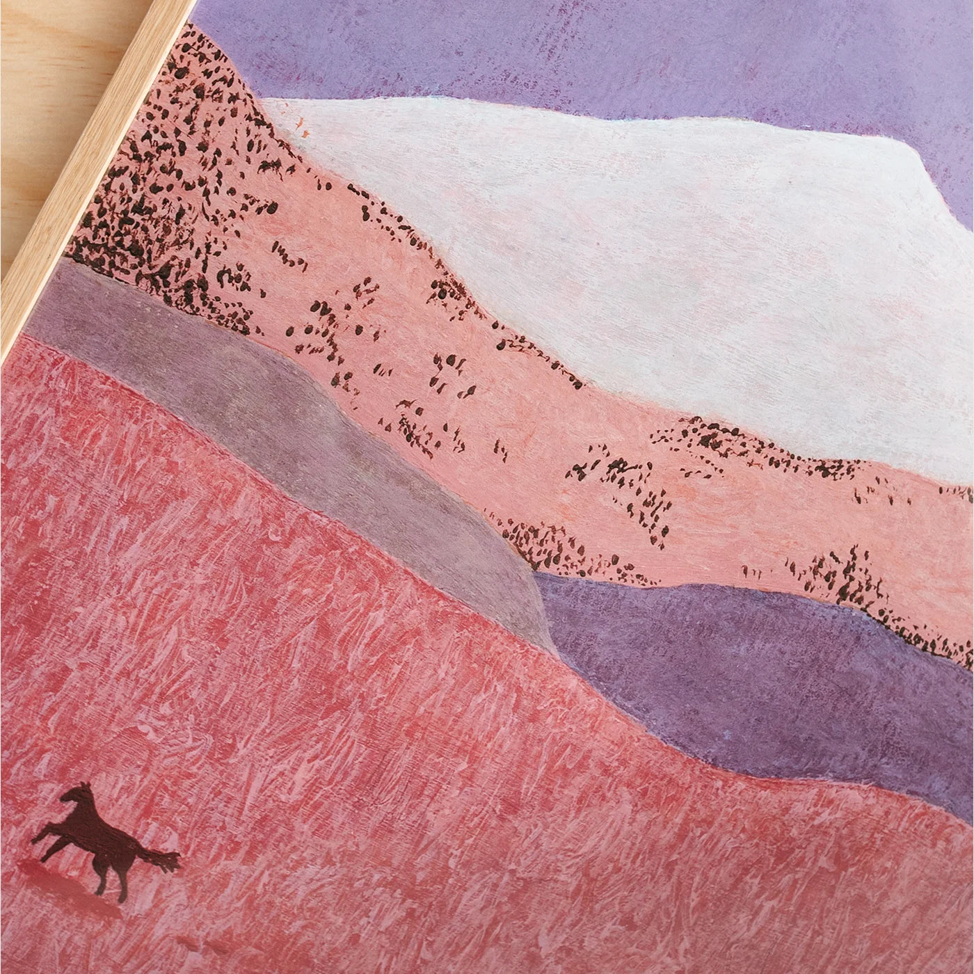 A textured art print depicting a stylized landscape with layered hills in pink, purple, and white, with a small dark horse silhouette galloping in the lower left, shown close up with a wooden edge visible at the top left.