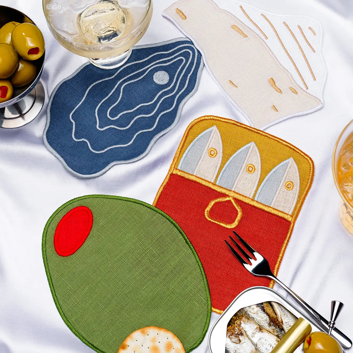 Set of fabric coasters with fish, cheese, olive, and oyster designs on a white surface.