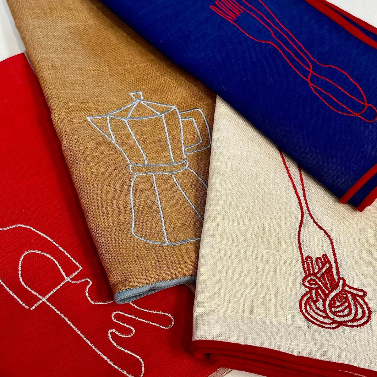 Four fabric napkins with embroidered designs on a flat surface