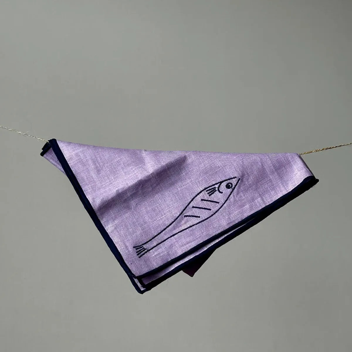 Purple fabric napkin with fish design hanging on a string against a gray background