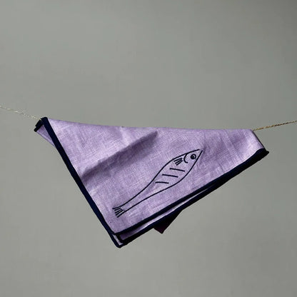 Purple fabric napkin with fish design hanging on a string against a gray background