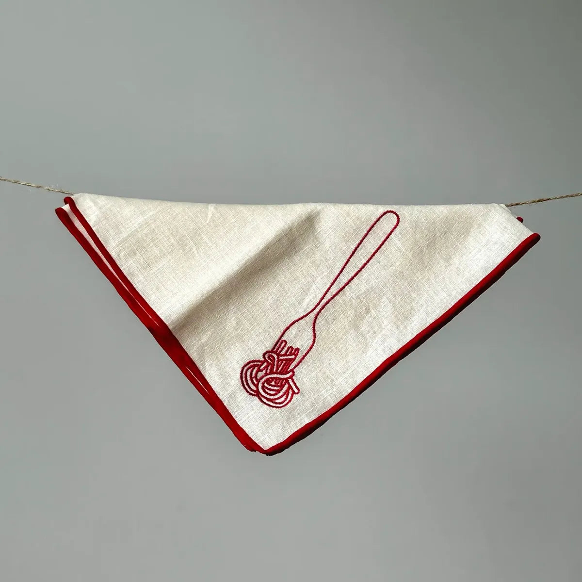 White napkin with red border and embroidered design on a gray background