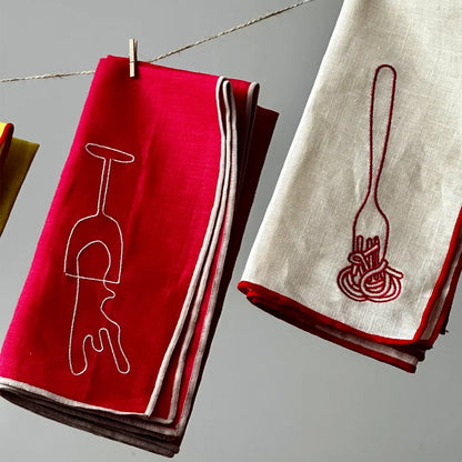 Red and beige napkins with embroidered designs on a gray background