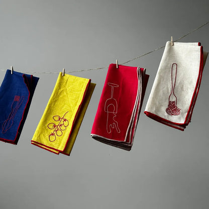 Four colorful napkins with embroidered designs hanging on a line against a gray background.