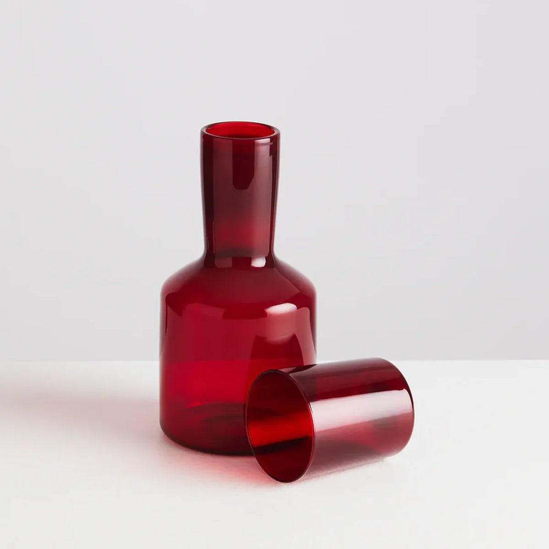 Red glass carafe and glass on a light gray background