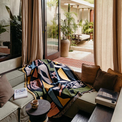 Living room with a colorful blanket on a sofa, large windows, and outdoor view.