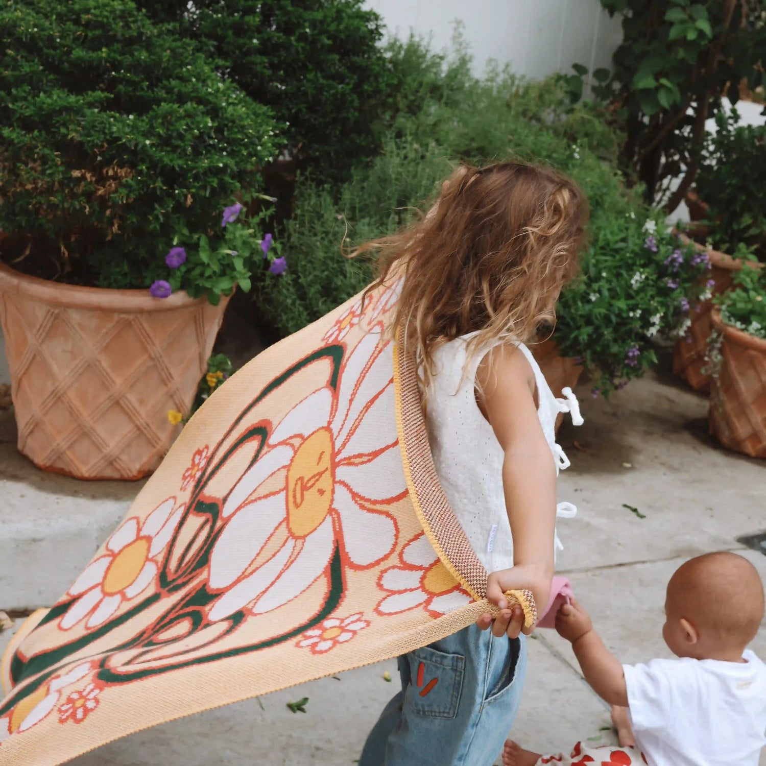 Children playing with colourful yellow baby blanket with flower character design on it