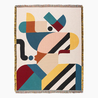 Slowdown Studio Pierre woven throw blanket with fringe on all sides, featuring an abstract geometric design in teal, mustard yellow, peach, burgundy, black, and cream on a light beige background.