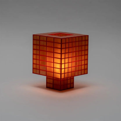 A Ridezign Tesser 8:3 table lamp with a translucent orange-red glass body and a glowing warm light inside, set against a neutral gray background.