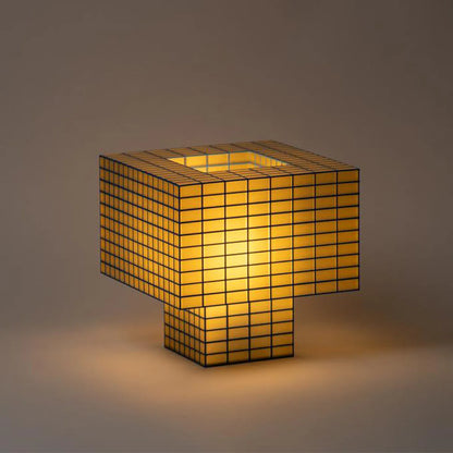 Illuminated Ridezign Tesser XL 5:3 lamp in Butter with an open top, made from a blue grid over warm yellow panels, casting a soft glow against a neutral grey-brown background.