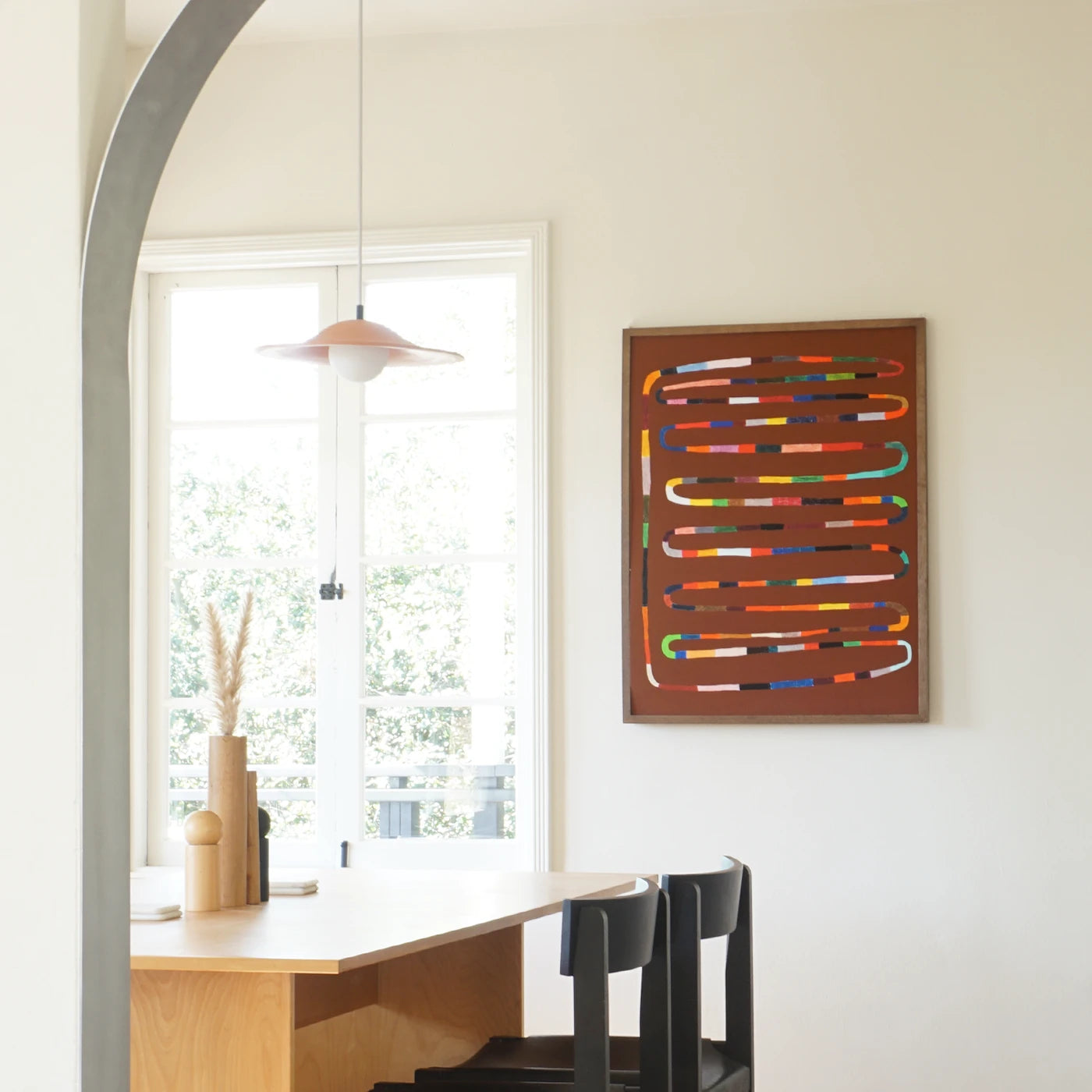 Kitchen wall art featuring a framed abstract artwork with colorful curved lines on a brown background, displayed on a white wall in a modern kitchen setting with a wooden table and chairs.