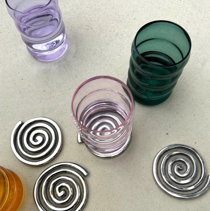 Colorful glass tumblers with spiral coasters on a light surface