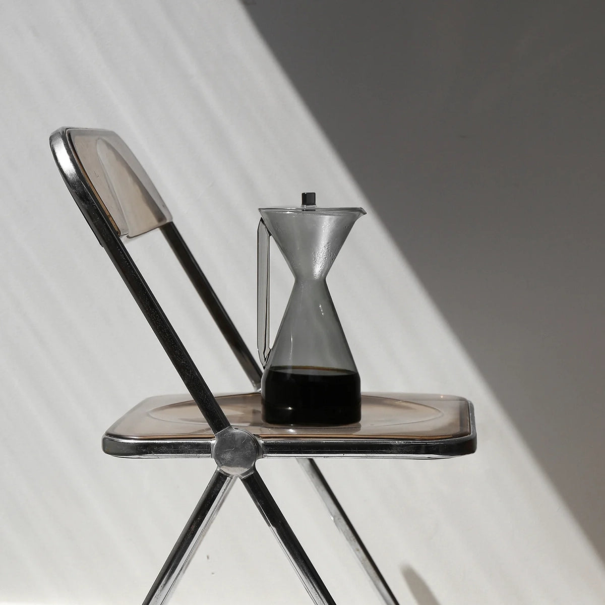 Gray glass hourglass-shaped carafe on a small metal chair with a white background