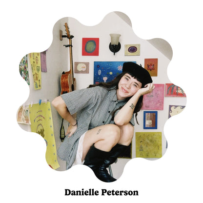 Portrait of American artist Danielle Peterson in her art studio in front of a wall of art